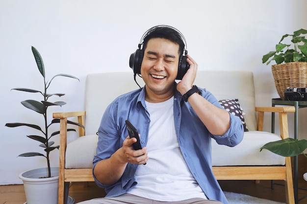 Giovane sorridente che usa il telefono per ascoltare musica seduto sul pavimento
