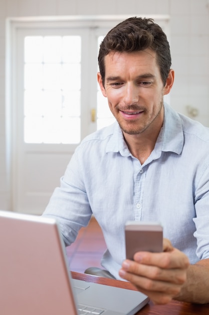 Giovane sorridente che utilizza computer portatile e telefono cellulare