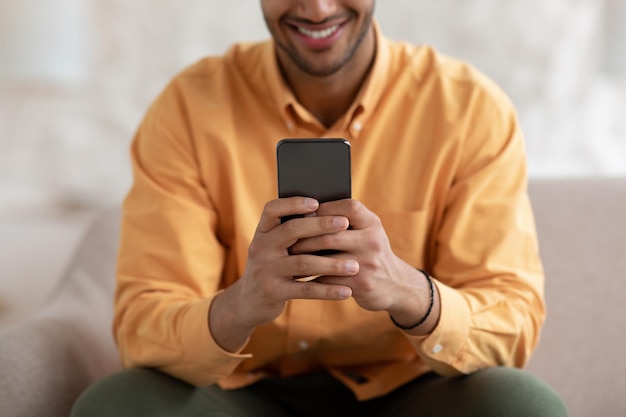 Giovane sorridente che utilizza smartphone a casa da vicino