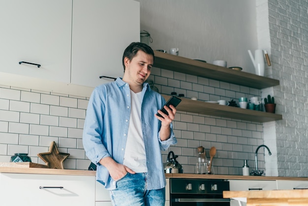 Giovane sorridente che utilizza smartphone in cucina