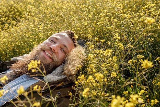 Giovane sorridente con una barba che si trova in un campo di fiori gialli