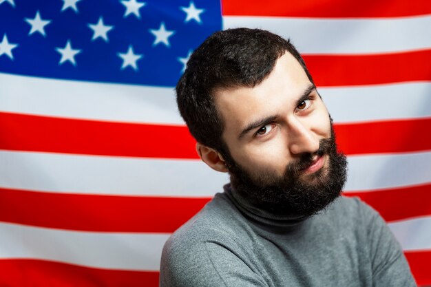 Giovane sorridente con una barba su uno sfondo della bandiera americana. Avvicinamento. Giorno dell'Indipendenza.