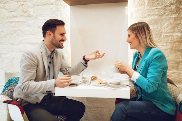 Giovane sorridente e giovane donna che parlano e che bevono caffè in un caffè.