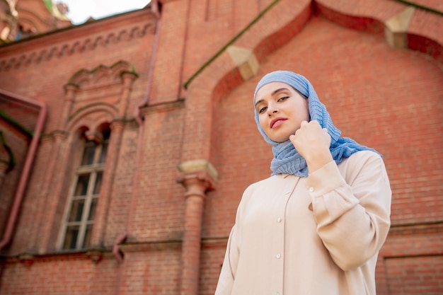 Giovane splendida donna araba in piedi sul muro dell'esterno del tempio orientale durante il viaggio nella città antica