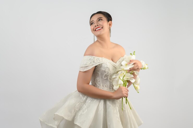 Giovane splendida sposa asiatica con un bouquet di orchidee su sfondo bianco