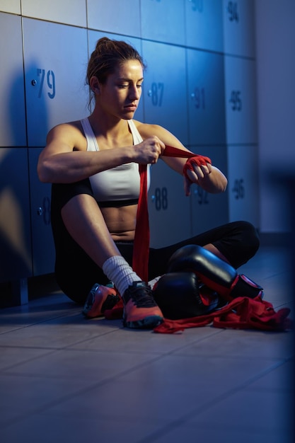 Giovane sportiva che si prepara per l'allenamento di boxe e avvolge le mani con una benda negli spogliatoi