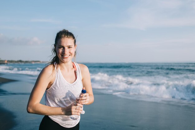 Giovane sportiva con bottiglia d'acqua sulla spiaggia