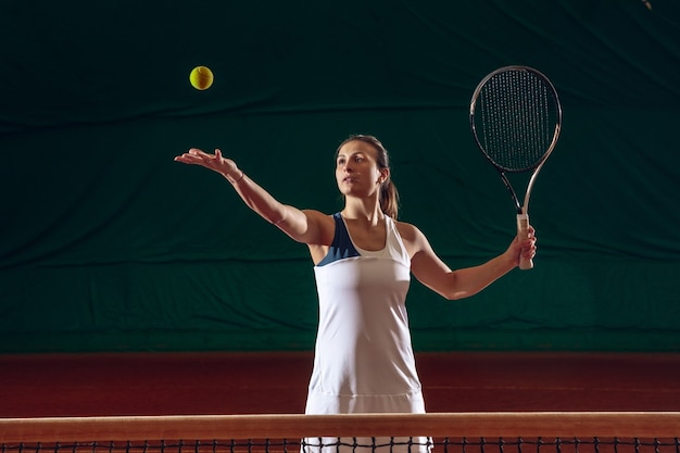 Giovane sportiva professionista giocando a tennis sulla parete del campo sportivo