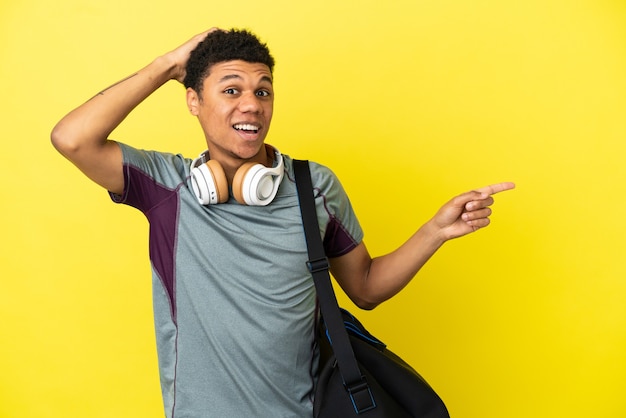 Giovane sportivo afroamericano con borsa sportiva isolata su sfondo giallo sorpreso e puntando il dito sul lato