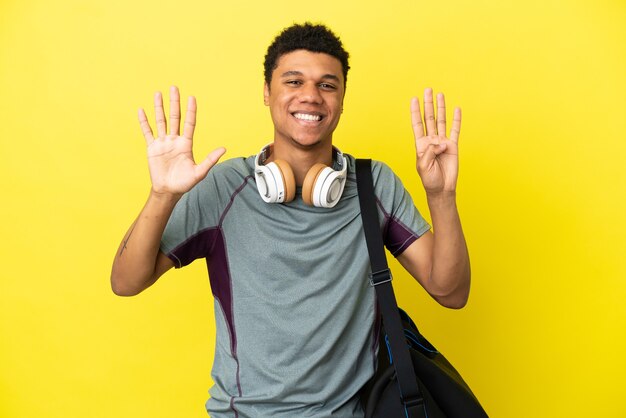 Giovane sportivo afroamericano con borsa sportiva isolato su sfondo giallo contando nove con le dita