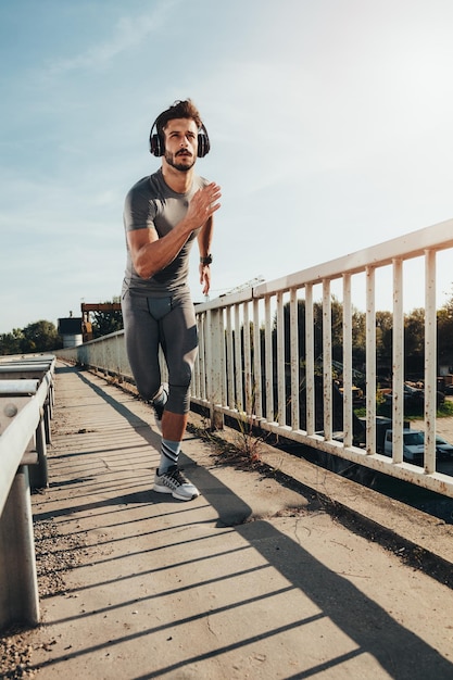 Giovane sportivo con le cuffie che pareggiano al ponte.