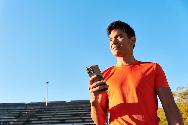 Giovane sportivo sorridente che tiene il suo smartphone Raggiungere il concetto di obiettivi