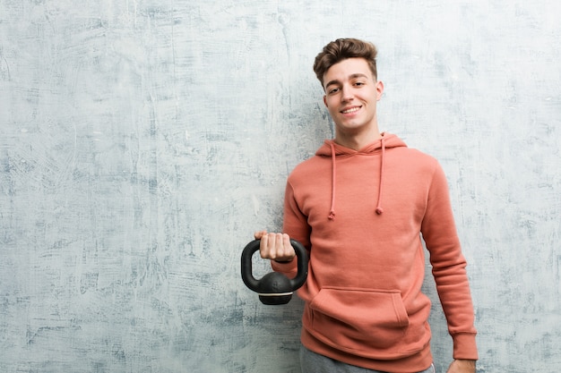 Giovane sportivo uomo che tiene un manubrio felice, sorridente e allegro.