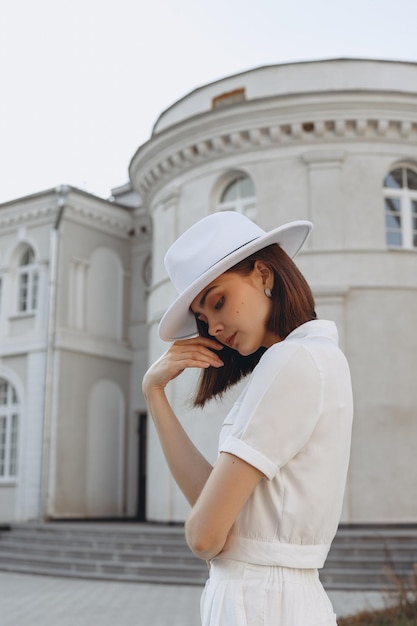 giovane sposa sognante in cappello di feltro bianco e camicetta elegante che guarda in basso