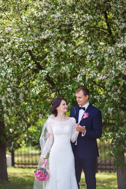 Giovane sposo e sposa con bouquet da sposa rosa nel giardino fiorito