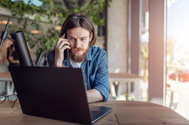 Giovane startupper casual che parla al cellulare mentre lavora con un laptop in un'area di lavoro loft