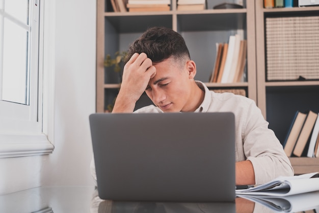 Giovane stressato malsano che soffre di mal di testa a casa a causa del superlavoro e dello studio duro per gli esami. Adolescente maschio stanco che fa i compiti per la scuola