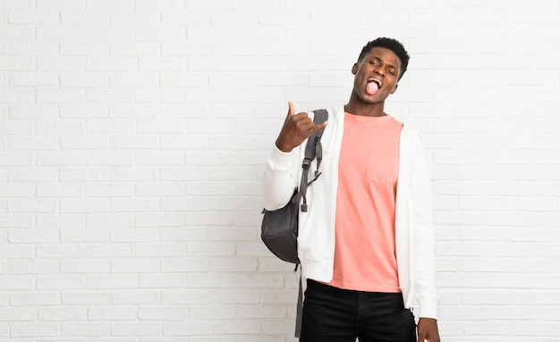 Giovane studente afro americano uomo mostrando la lingua alla fotocamera con sguardo divertente