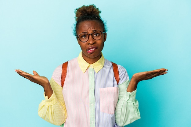 Giovane studente americano africano donna su sfondo isolato confuso e dubbioso alzando le spalle per tenere una copia dello spazio.