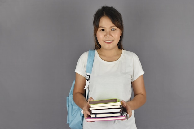 Giovane studente asiatico che sorride con lo zaino e che tiene i libri.