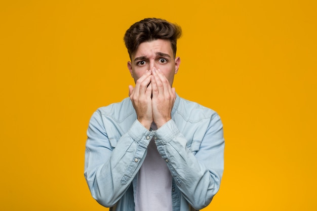 Giovane studente bello che indossa una camicia di jeans spaventato e impaurito.