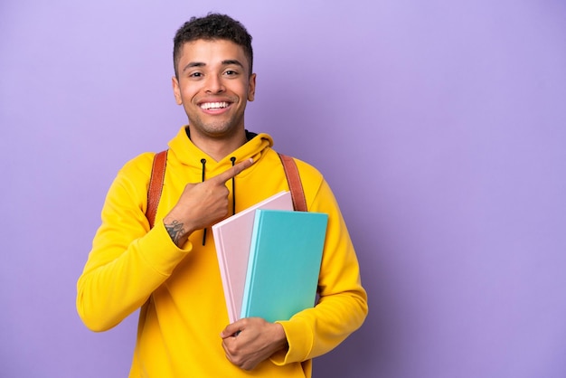 Giovane studente brasiliano uomo isolato su sfondo viola che indica il lato per presentare un prodotto