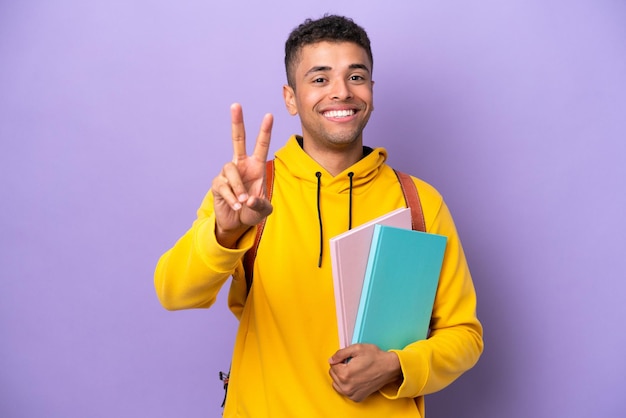 Giovane studente brasiliano uomo isolato su sfondo viola sorridente e mostrando il segno di vittoria