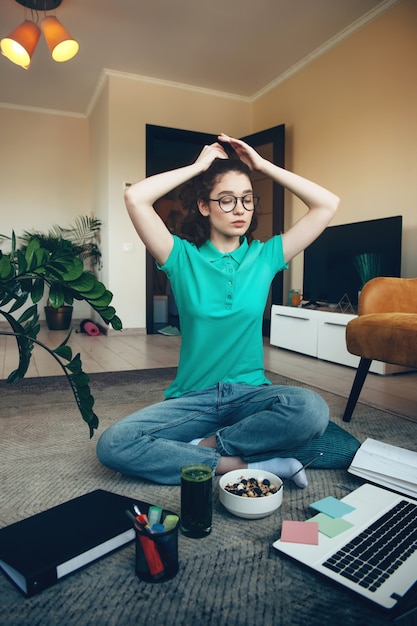 Giovane studente che si prepara per le lezioni online seduto sul pavimento con un laptop e un piatto di cereali