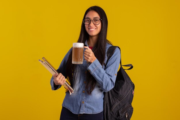 Giovane studente che tiene zaino e libri e un bicchiere di birra in studio girato