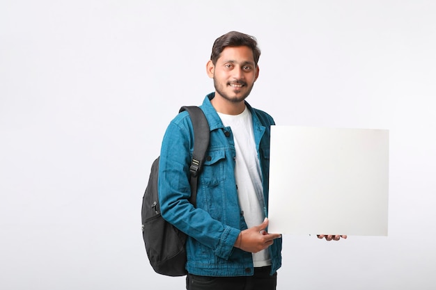 Giovane studente di college indiano che mostra il cartello in bianco su sfondo bianco.