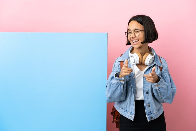 Giovane studente di razza mista donna con un grande striscione su sfondo isolato che punta verso la parte anteriore e sorridente