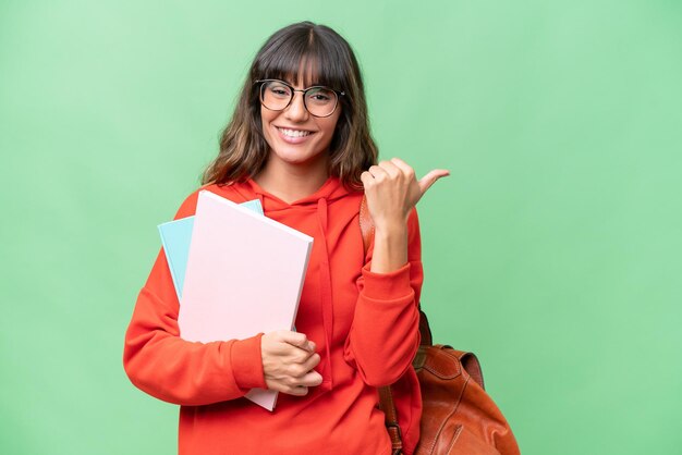 Giovane studente donna caucasica su sfondo isolato che punta al lato per presentare un prodotto