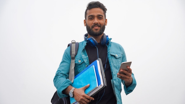 Giovane studente felice con libri e laptop utilizzando il cellulare