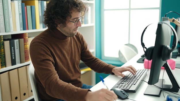 Giovane studente ispanico che utilizza il computer che scrive sul taccuino all'università della biblioteca