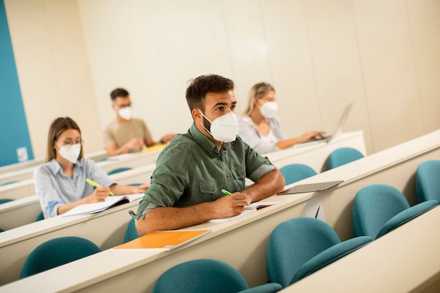 Giovane studente maschio che indossa la maschera medica protettiva per il viso per la protezione da virus in aula