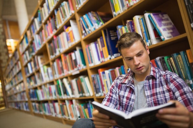 Giovane studente messo a fuoco che si siede sul libro di lettura del pavimento delle biblioteche