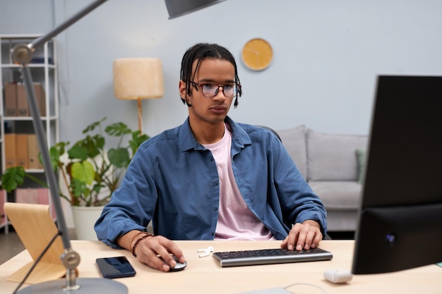 Giovane studente nero che utilizza il computer a casa e scrive codice online