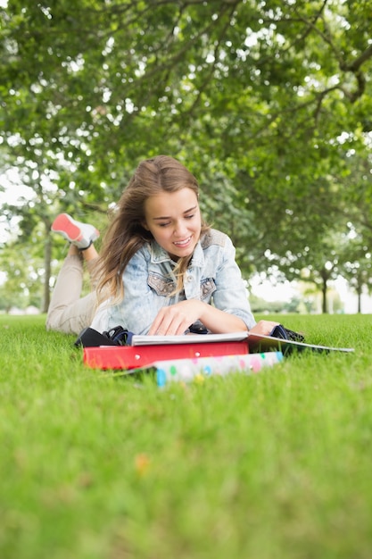 Giovane studente sorridente che studia sull&#39;erba