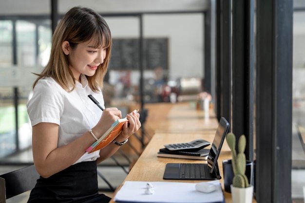 Giovane studente universitario asiatico attraente che scrive nota e utilizza il computer per imparare online