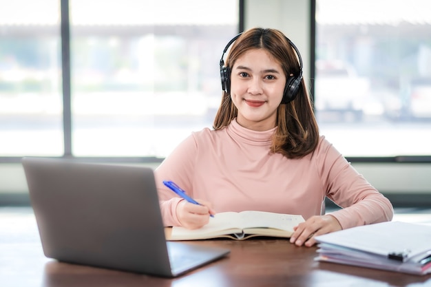 Giovane studente universitario indossa le cuffie e scrive sul notebook mentre studia online tramite il laptop a casa