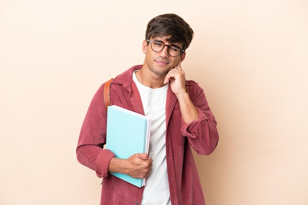 Giovane studente uomo caucasico isolato su sfondo ocra frustrato e che copre le orecchie