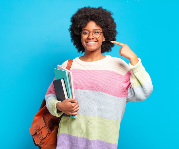 Giovane studentessa afro che sorride fiduciosamente indicando il proprio ampio sorriso, atteggiamento positivo, rilassato e soddisfatto