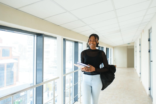 Giovane studentessa afroamericana sorridente felice a piedi al campus universitario