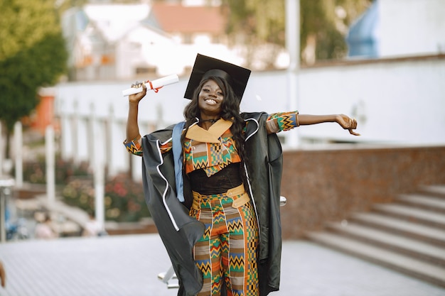 Giovane studentessa afroamericana vestita in abito nero di graduazione. Campus come sfondo