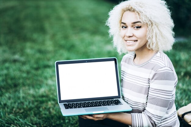 Giovane studentessa allegra detiene un computer portatile con uno schermo bianco