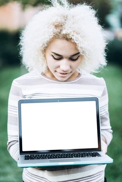 Giovane studentessa allegra detiene un computer portatile con uno schermo bianco