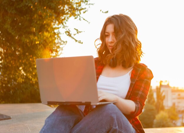 Giovane studentessa allegra seduta con il computer portatile all'aperto al mattino presto all'alba