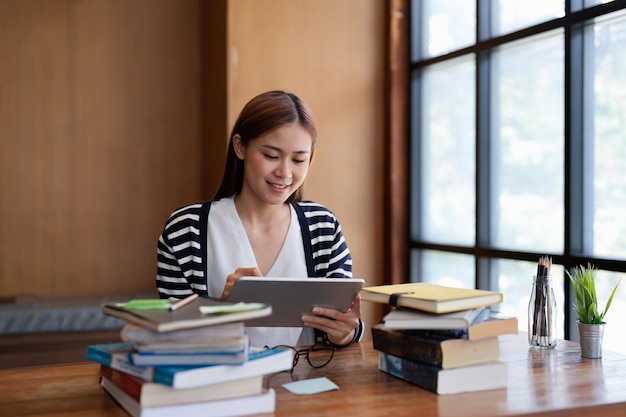 Giovane studentessa asiatica che lavora alla compressa digitale in biblioteca