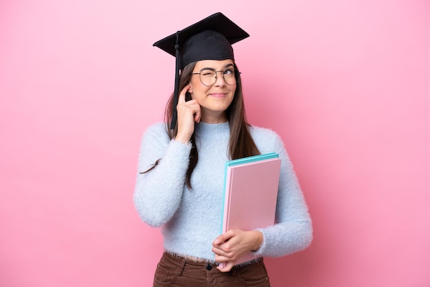 Giovane studentessa brasiliana che indossa un cappello laureato isolato su sfondo rosa frustrata e che copre le orecchie