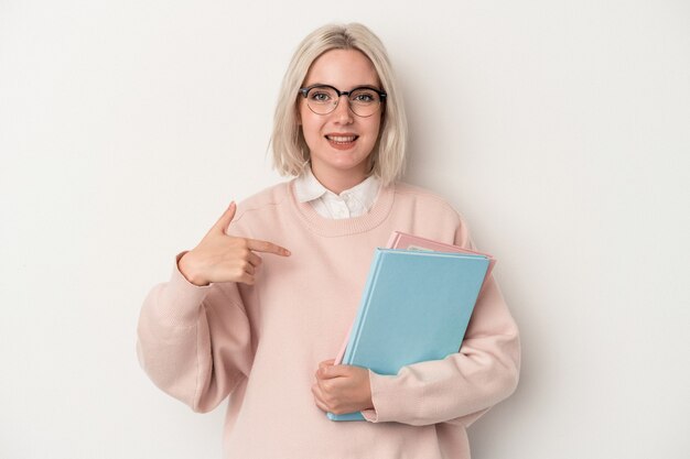 Giovane studentessa caucasica che tiene in mano libri isolati su sfondo bianco persona che indica a mano uno spazio per la copia della camicia, orgogliosa e sicura di sé